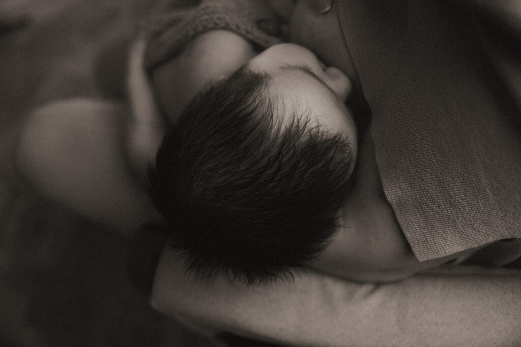 Black and white photograph of a newborn resting peacefully in a mother’s arms, captured during an in-home lifestyle session by Angela Wolf Photography in Las Vegas.