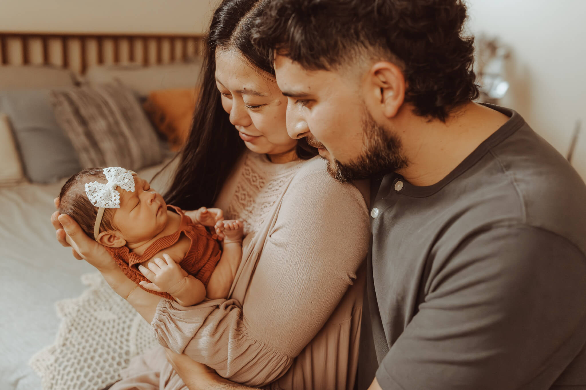 Las Vegas in-home newborn photography — parents lovingly holding baby girl with lace bow during lifestyle session by Angela Wolf Photography.